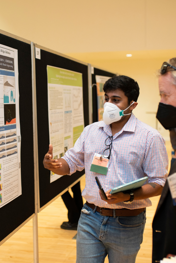 A student presenting his research to a judge through a poster on a temporary wall.
